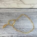 Gold heart carabiner bracelet with feather charm, top view
