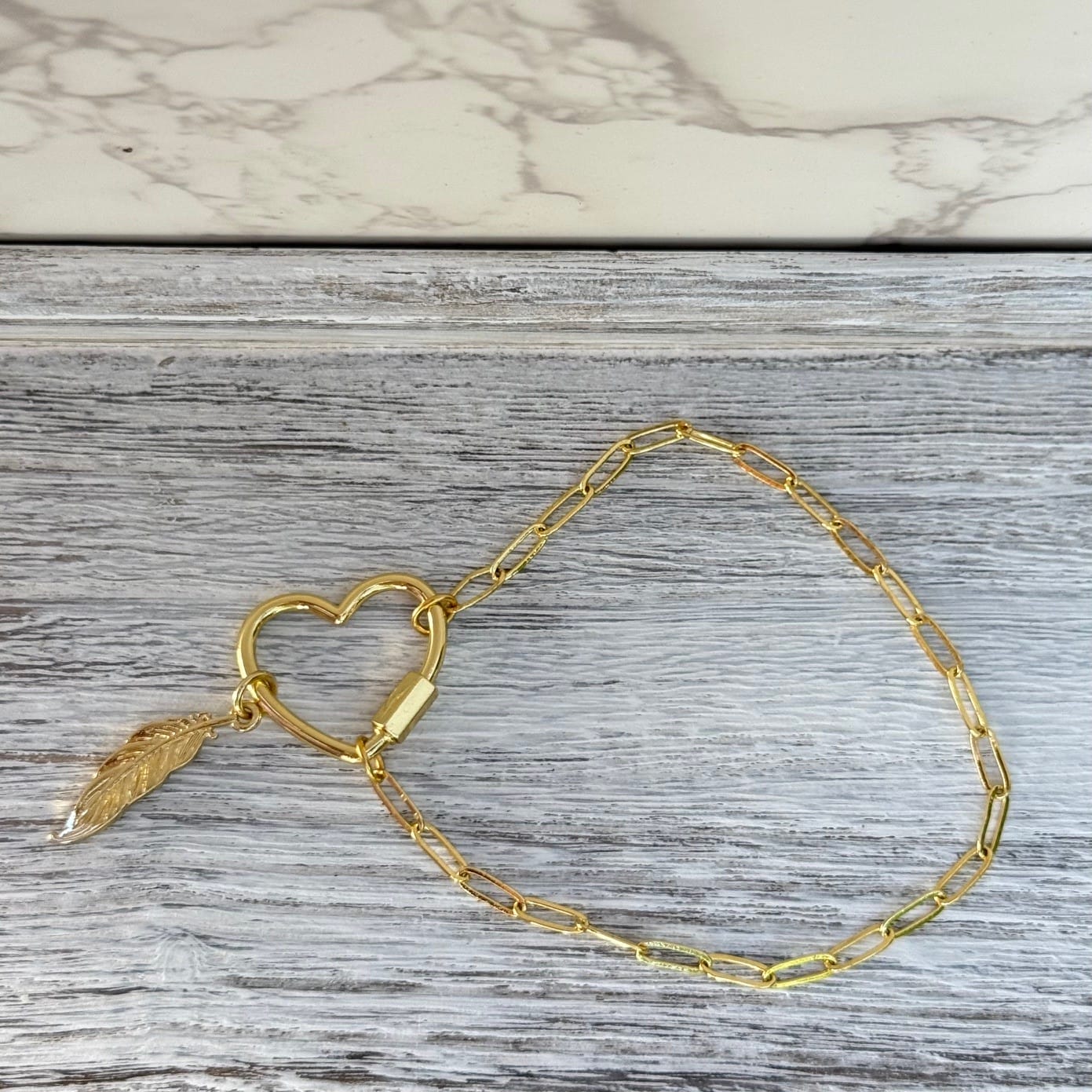 Gold heart carabiner bracelet with feather charm, top view